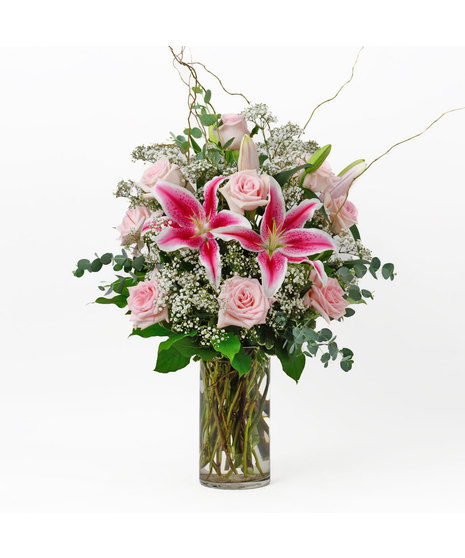 Long stem red roses, stargazer lilies, baby's breath and willow branches in a red glass vase.