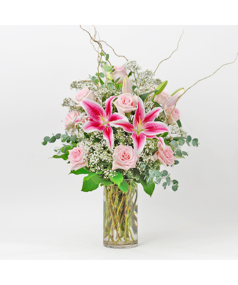 Long stem red roses, stargazer lilies, baby's breath and willow branches in a red glass vase.